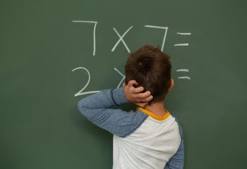 Rear view of Caucasian schoolboy doing math on greenboard in a classroom at elementary school